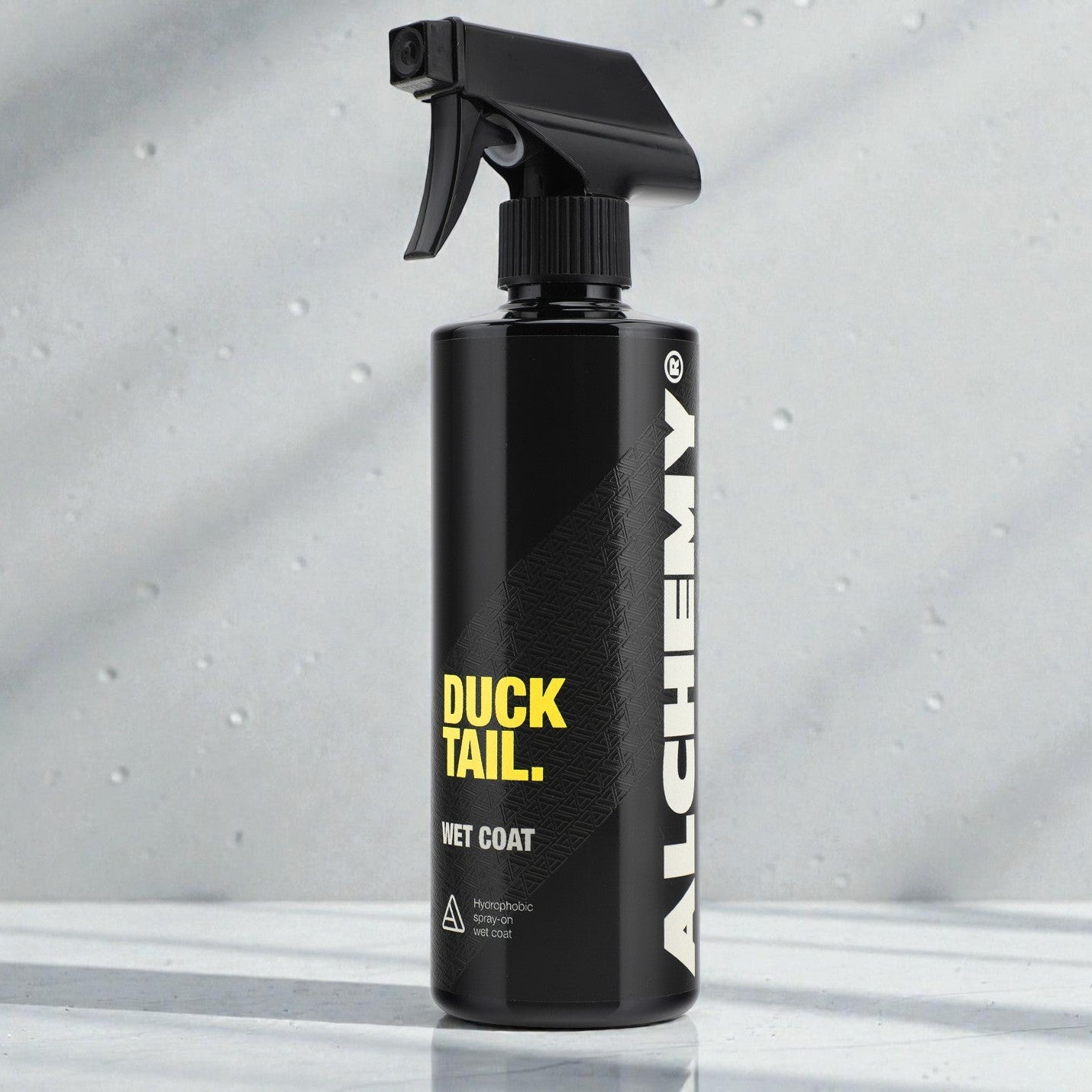 Black spray bottle labeled 'Duck Tail' and 'Alchemy' on a gray background