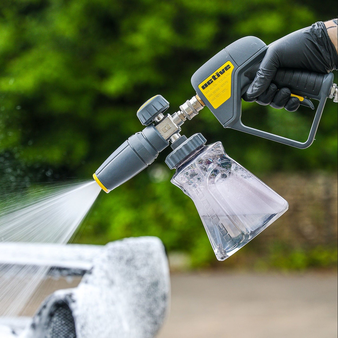 Active™ Premium Foam Cannon being used to clean a car with a blurred green outdoor background