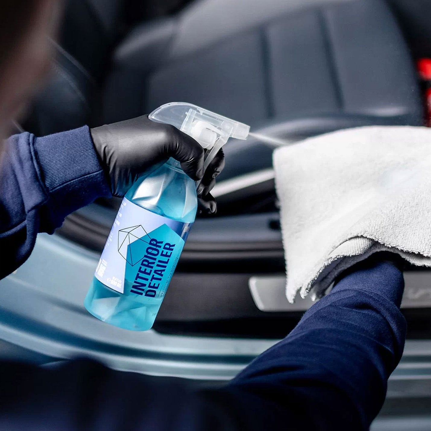 Person cleaning car interior with a spray bottle labeled 'Interior Detailer' and a white towel.