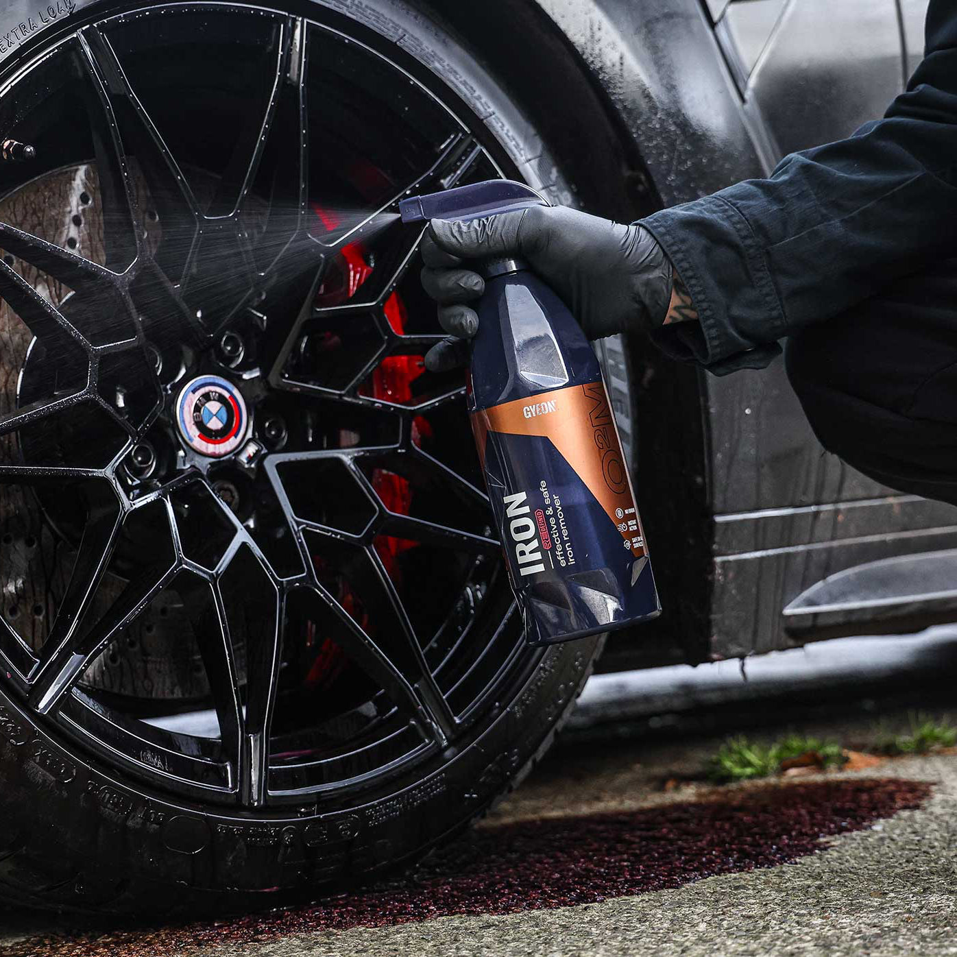 Person cleaning a car wheel with a bottle labeled 'IRON' near a BMW logo.