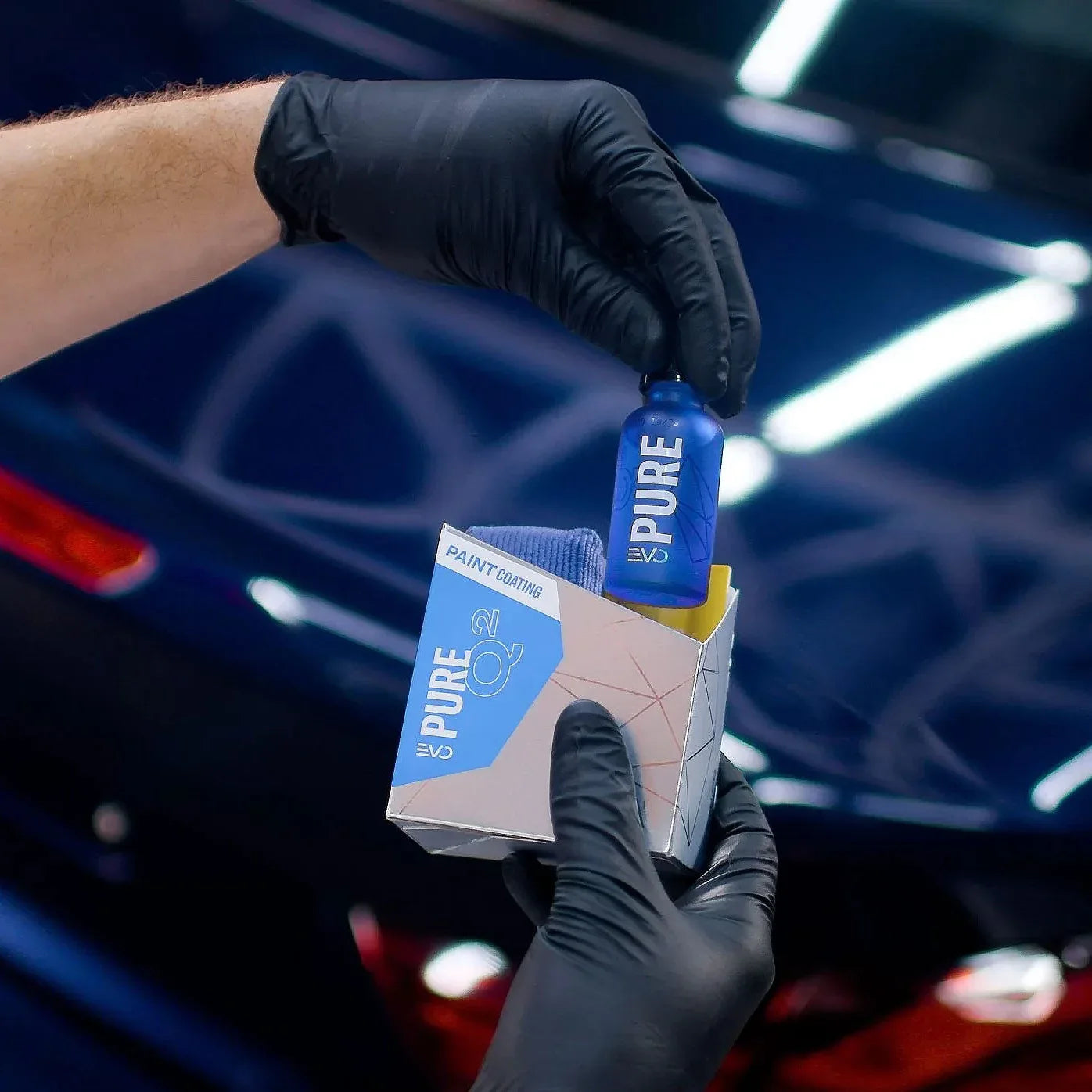 Person holding a blue bottle and white box labeled 'PURE' in front of a car interior.