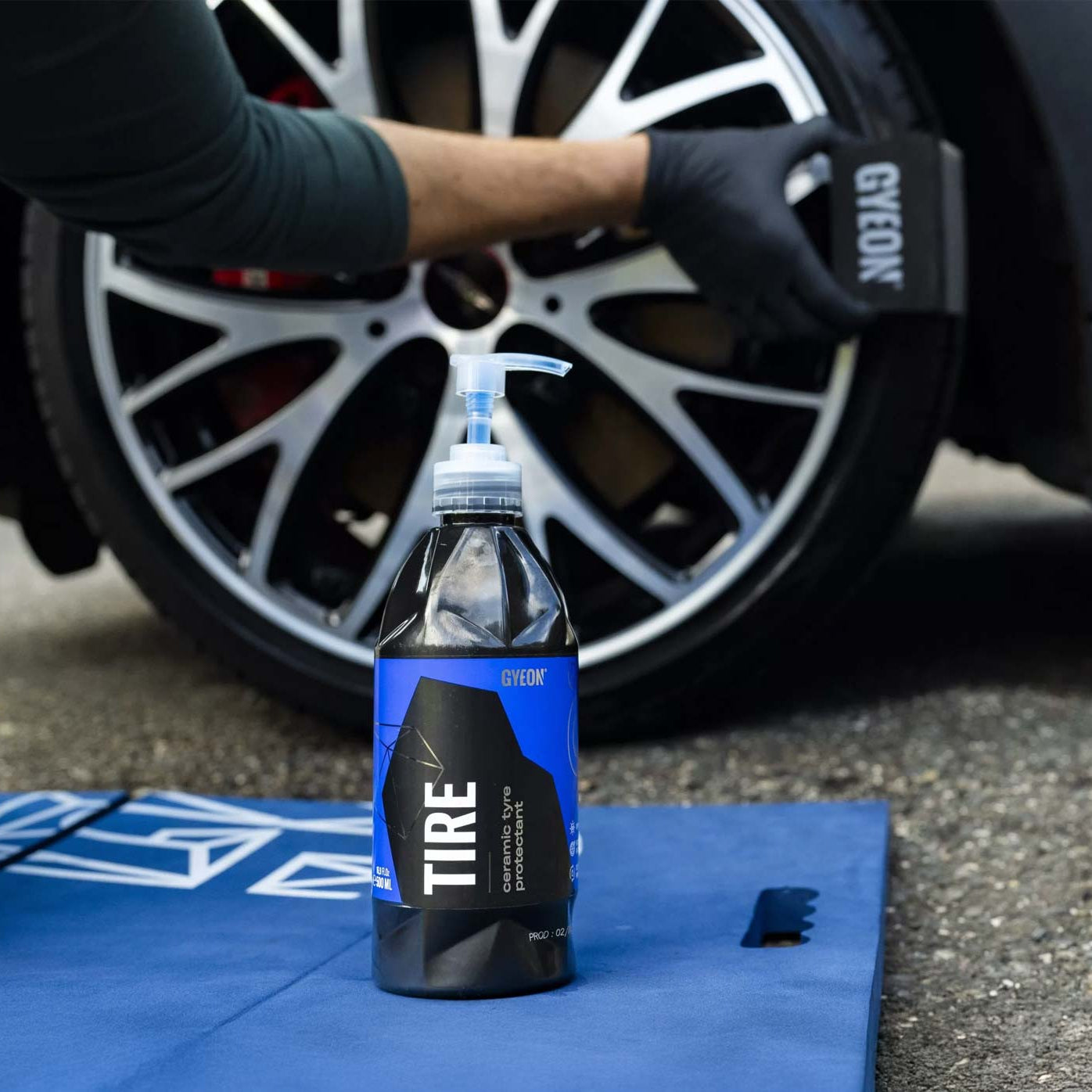 Bottle of GYEON tire product on a blue mat with a car tire in the background
