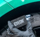 Gyeon tyre dressing applicator held by a gloved hand in front of a green car.