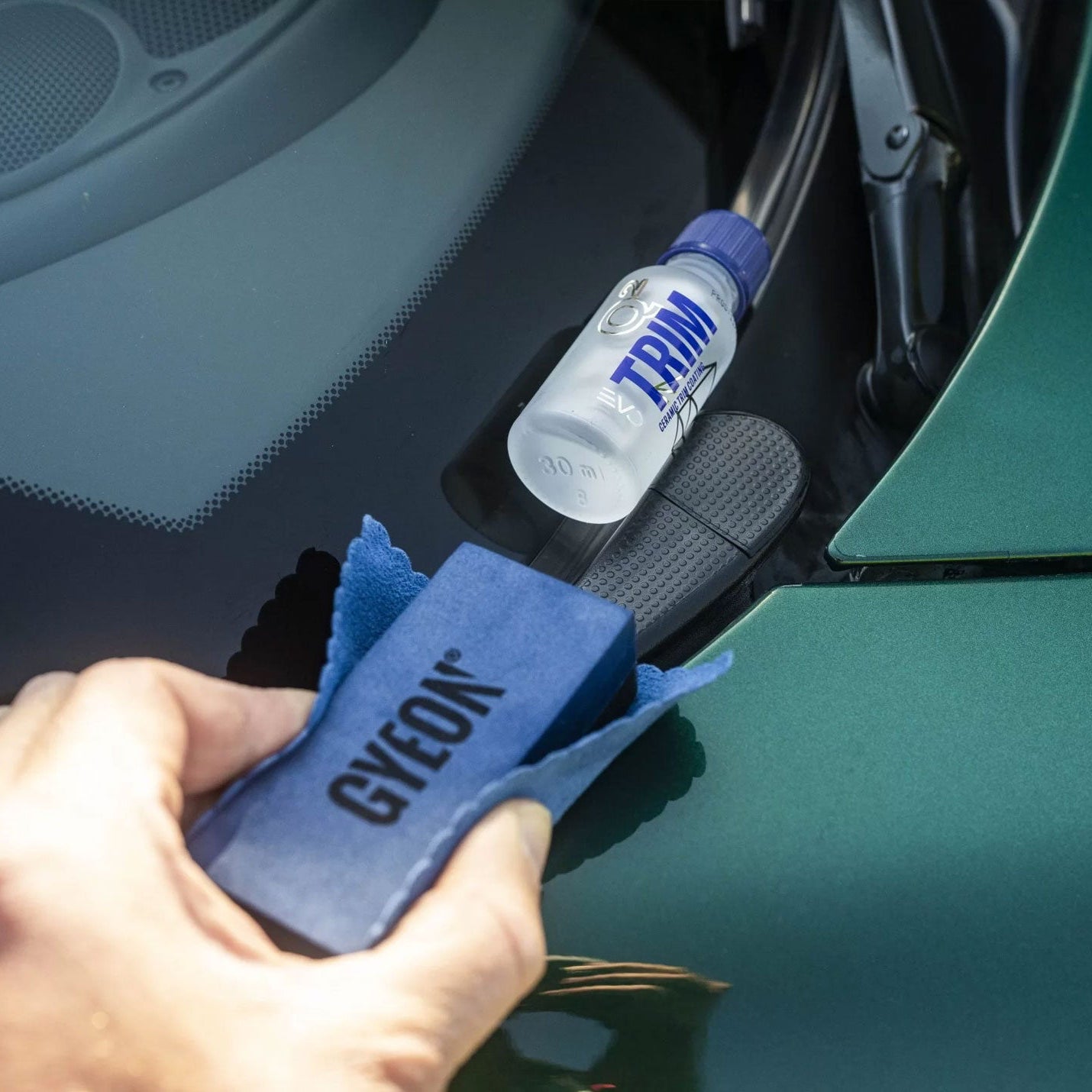 Person using a GYEON trim on a car's trim with a Gyeon applicator block & cloth in foreground.