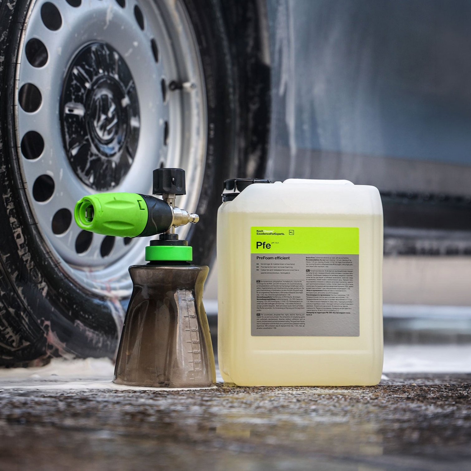 Koch-Chemie PreFoam Efficient alkaline pre-cleaner in a plastic container next to a foam cannon on a wet driveway.