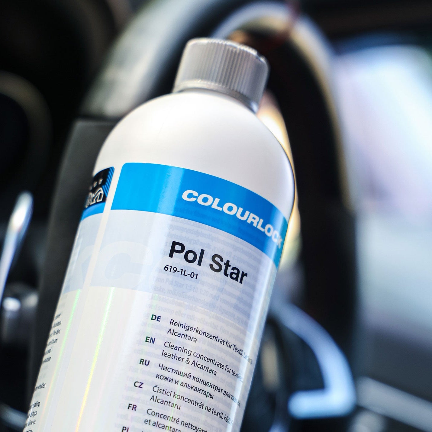 A bottle of Colourlock Pol Star car polish with a white label and blue accent band, shown in a close-up shot against a blurred car interior background.