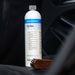 A bottle of Colourlock Pol Star car polish stands on a dark car seat, with a small wooden brush resting beside it. The background is a blurred car interior.