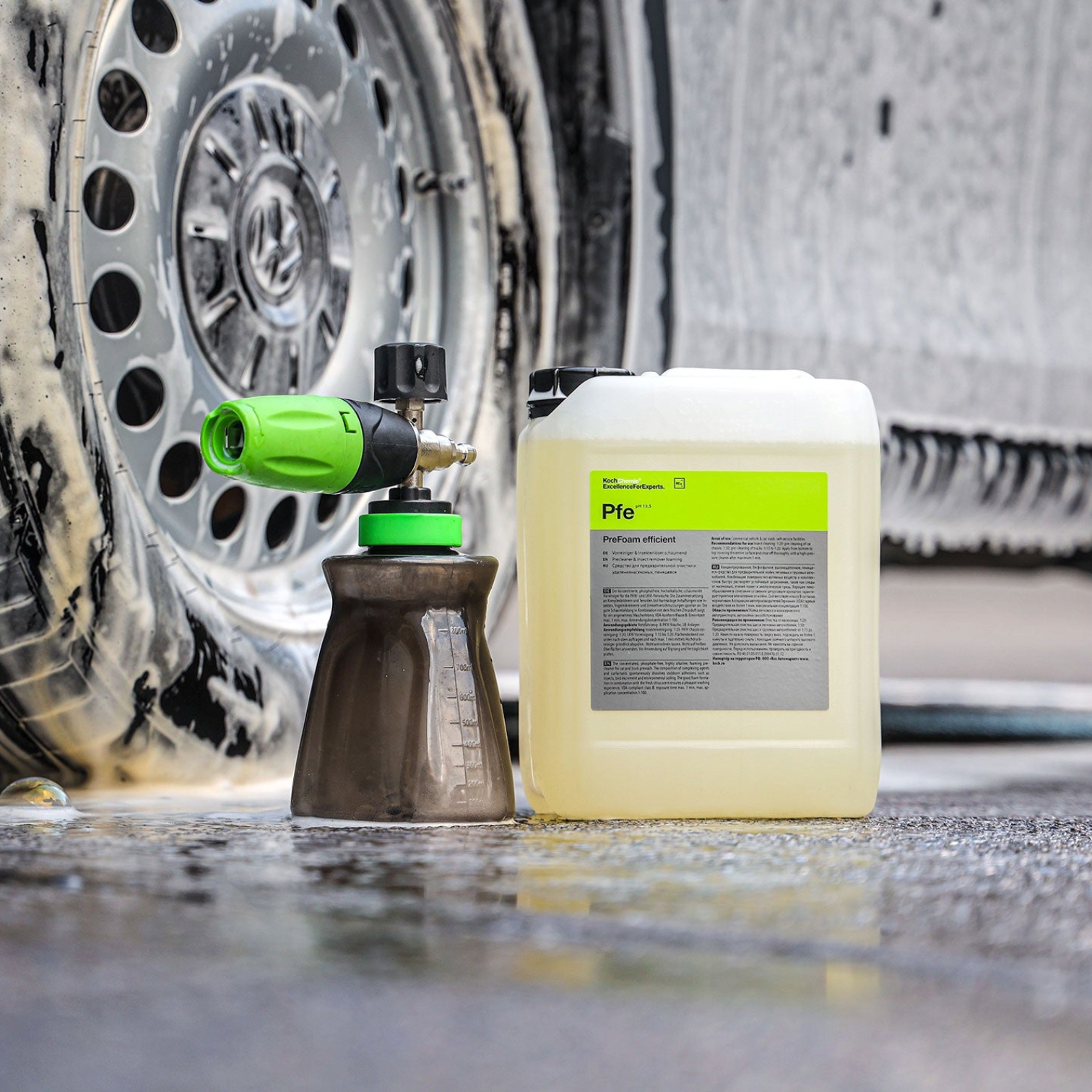 Koch-Chemie PreFoam Efficient alkaline pre-wash cleaner in a plastic container next to a foam cannon on a car wheel.