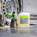 Koch-Chemie PreFoam Efficient alkaline pre-wash cleaner in a plastic container next to a foam cannon on a car wheel.