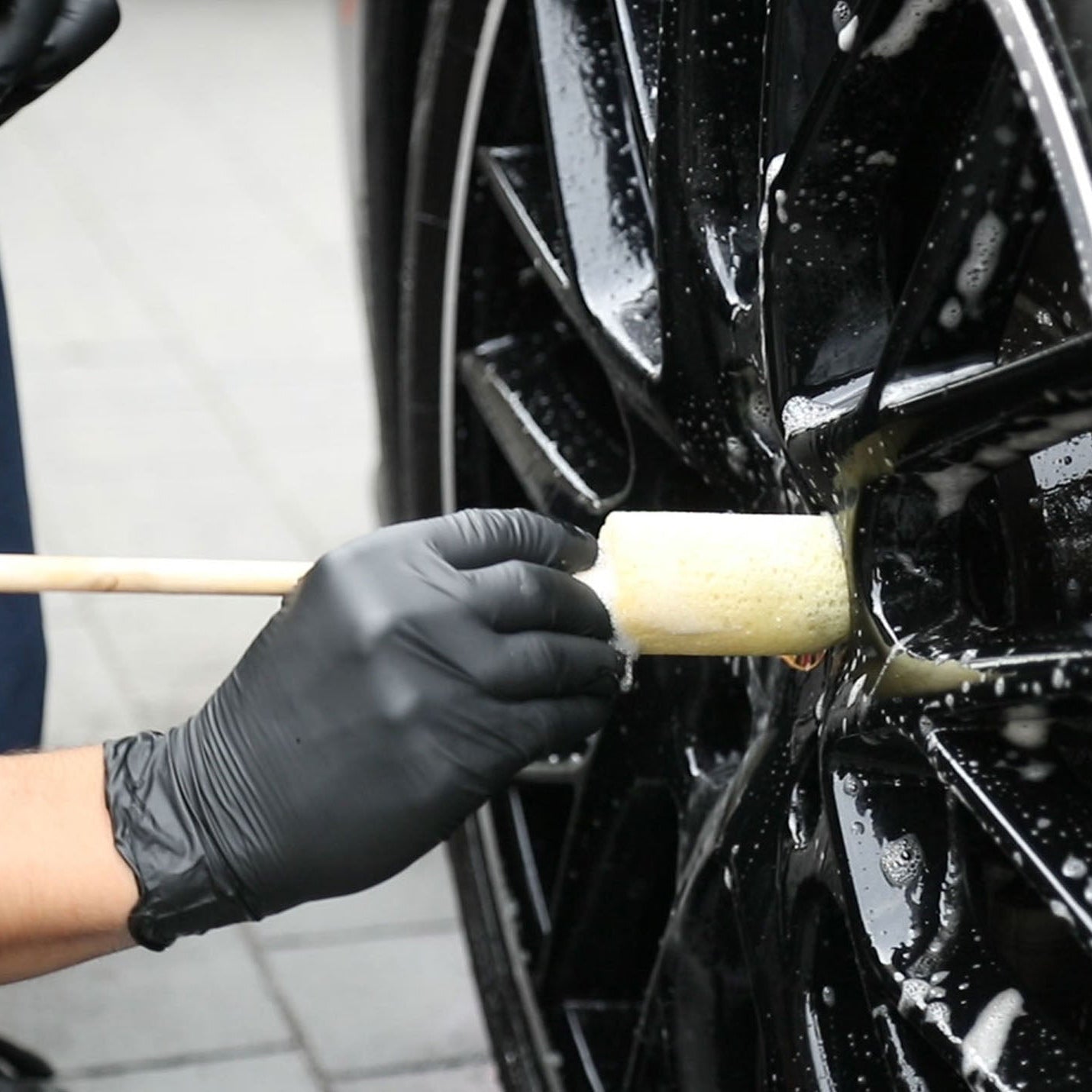 Person cleaning a car wheel with a sponge guru wheel brush