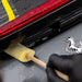 Person cleaning a car's taillight with a Sponge Guru Oval Wheel Brush, showing a horse emblem on the car.