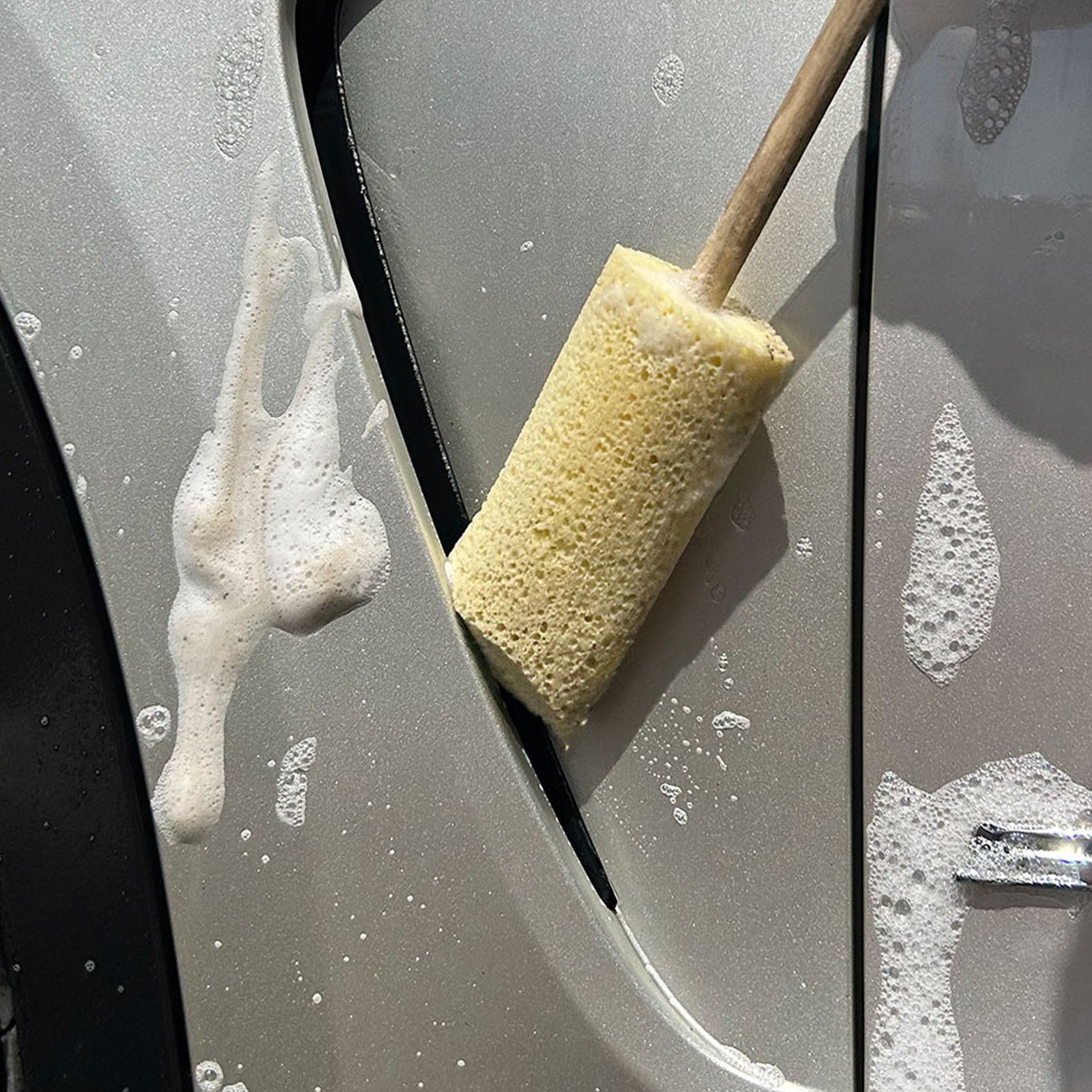 Sponge Guru Oval Wheel Brush on a car door with visible soap suds