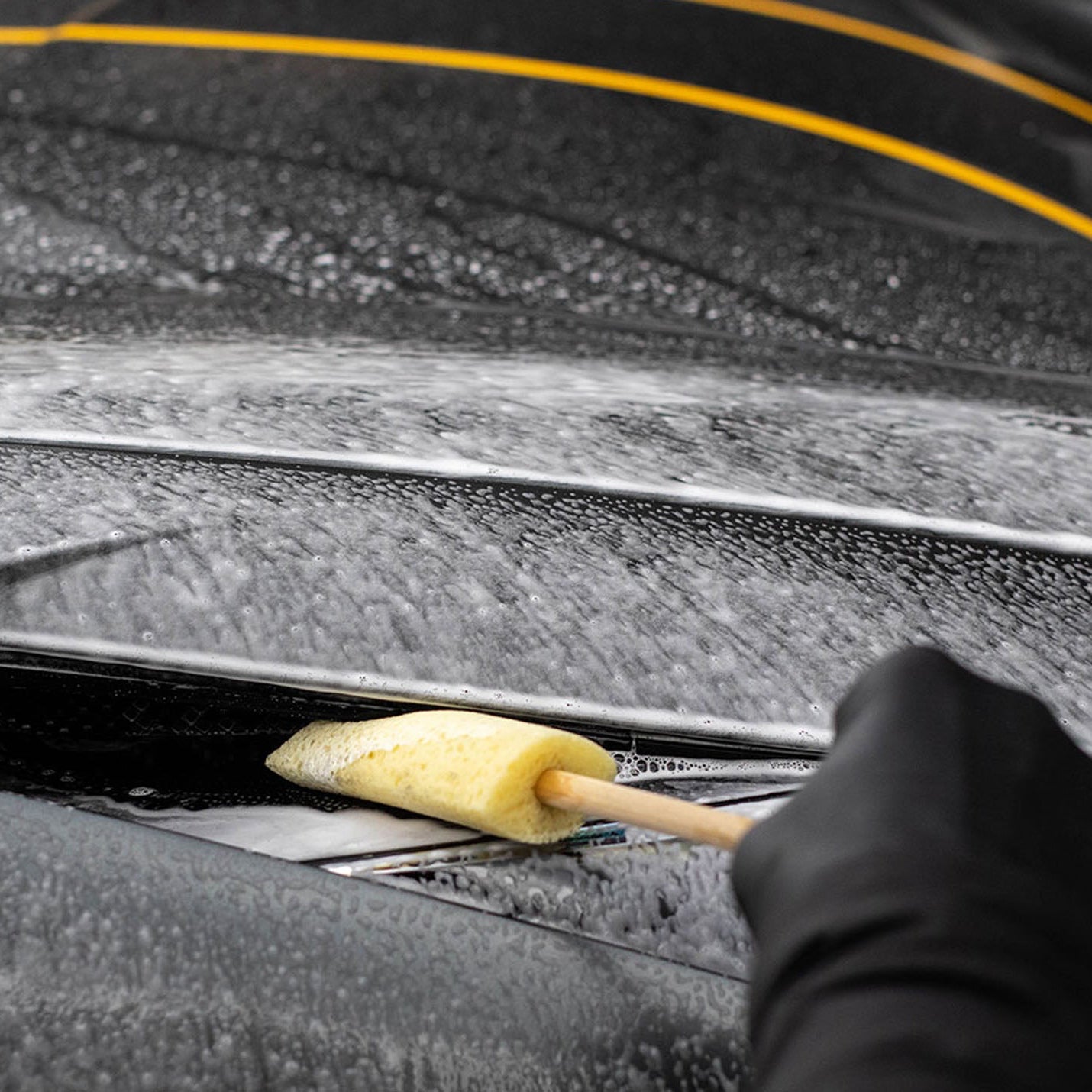 Person cleaning car windows with a Sponge Guru Oval Wheel Brush, focusing on the action of cleaning.